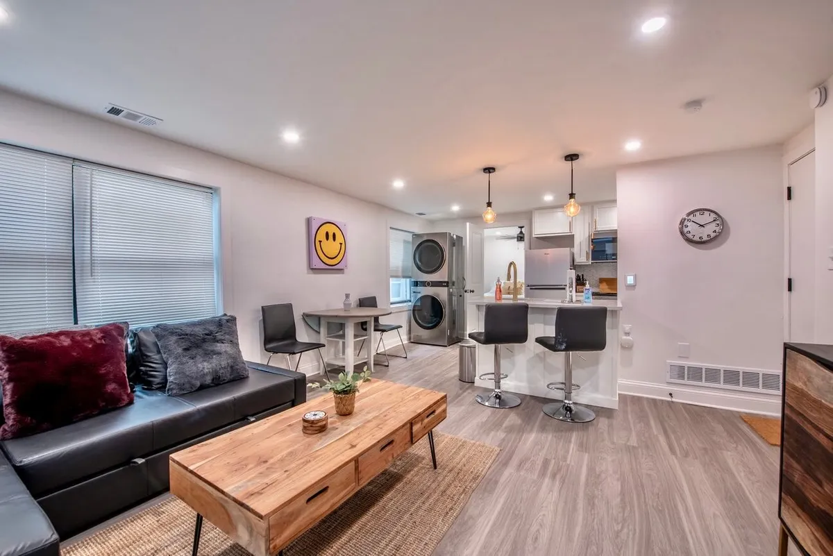 This image captures a seamless open-concept space, integrating the sofa, coffee table, kitchen island, and dining table within one cohesive area. Natural light streams in, illuminating the modern furnishings and clean lines. The arrangement supports both relaxation and socializing, with areas for enjoying a meal, lounging, or hosting friends.