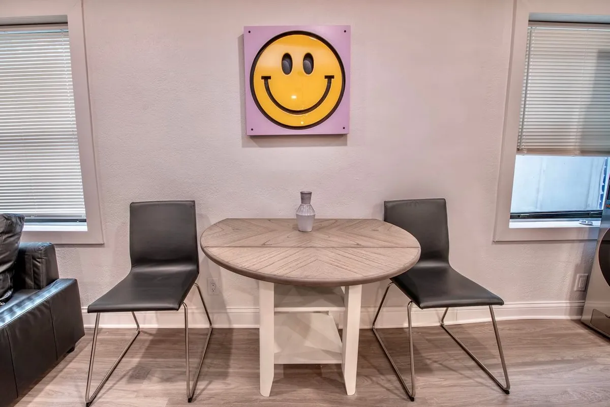 A bright, airy dining nook with modern chairs gathered around a round table, accented by playful smiley face wall art. The space is designed for casual dining and relaxed conversations, creating a welcoming spot for coffee gatherings or shared meals.